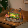 Maquette de tramway éclairée sur des rails avec des cerisiers en fleurs et des poteaux électriques.