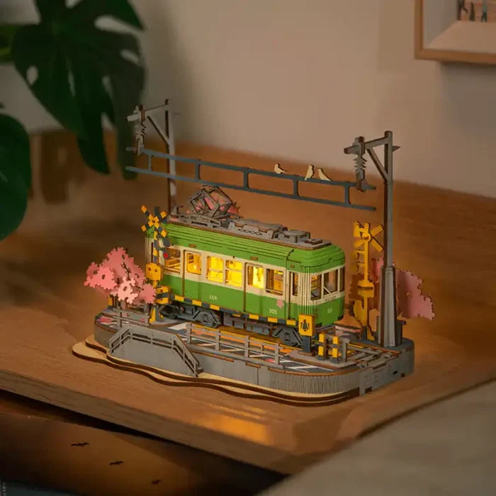 Maquette de tramway éclairée sur des rails avec des cerisiers en fleurs et des poteaux électriques.