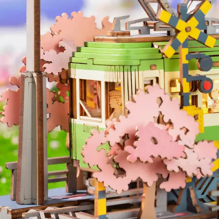 Scène miniature en papier craft représentant un bâtiment vert avec des cerisiers roses en fleurs.